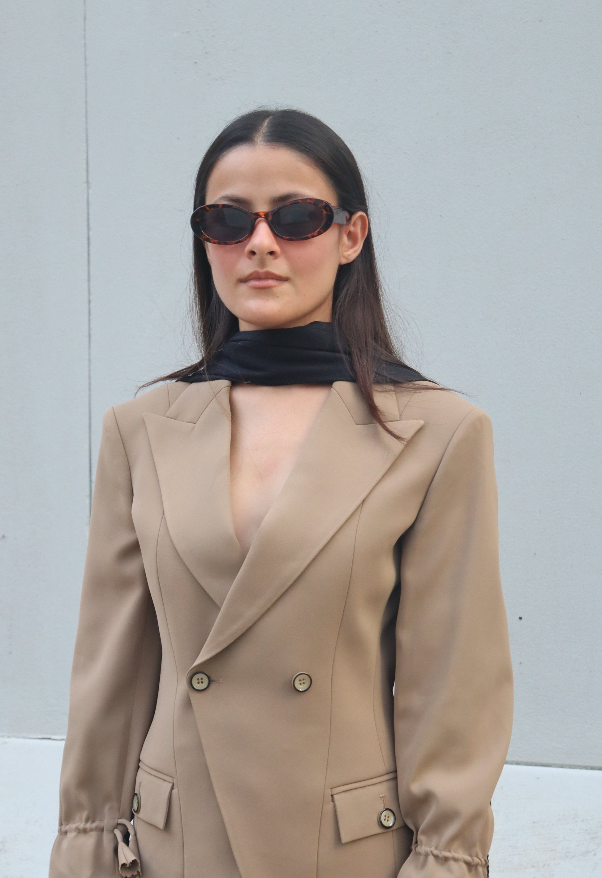 Woman wearing a beige trench coat and sunglasses on a city street.