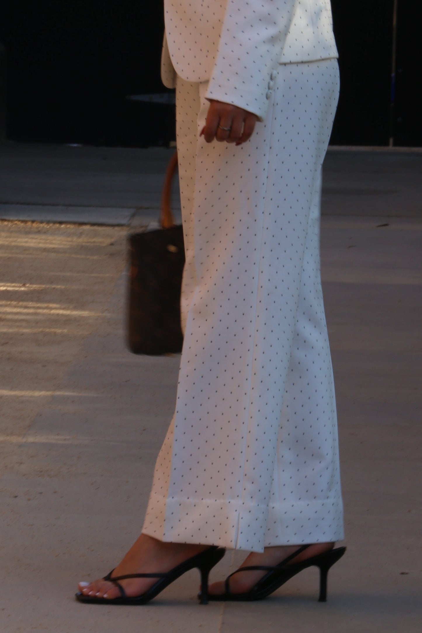 Person wearing white pants and black sandals standing against a wall with a vehicle in the background.